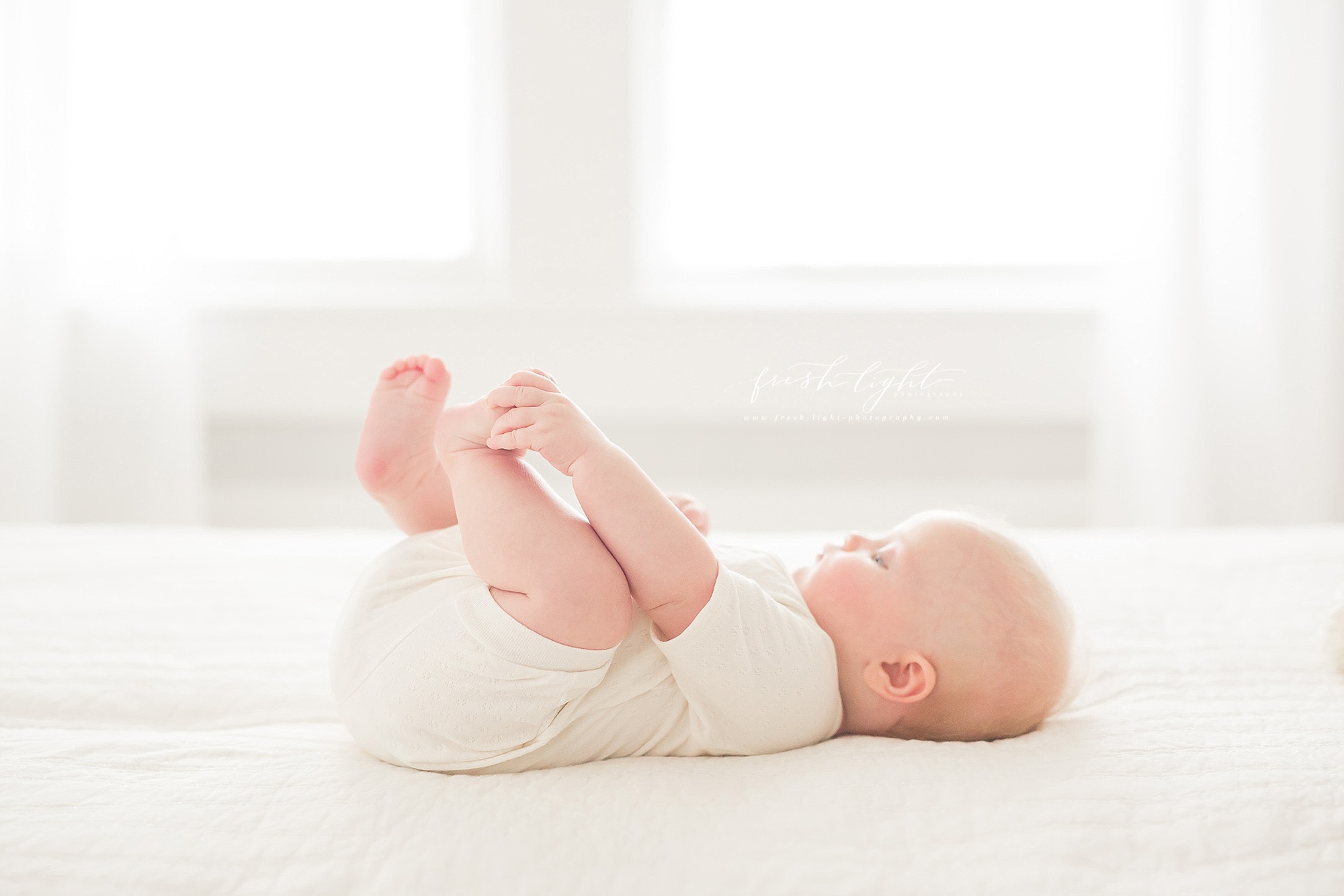 3 month old baby grabbing her toes on the bed