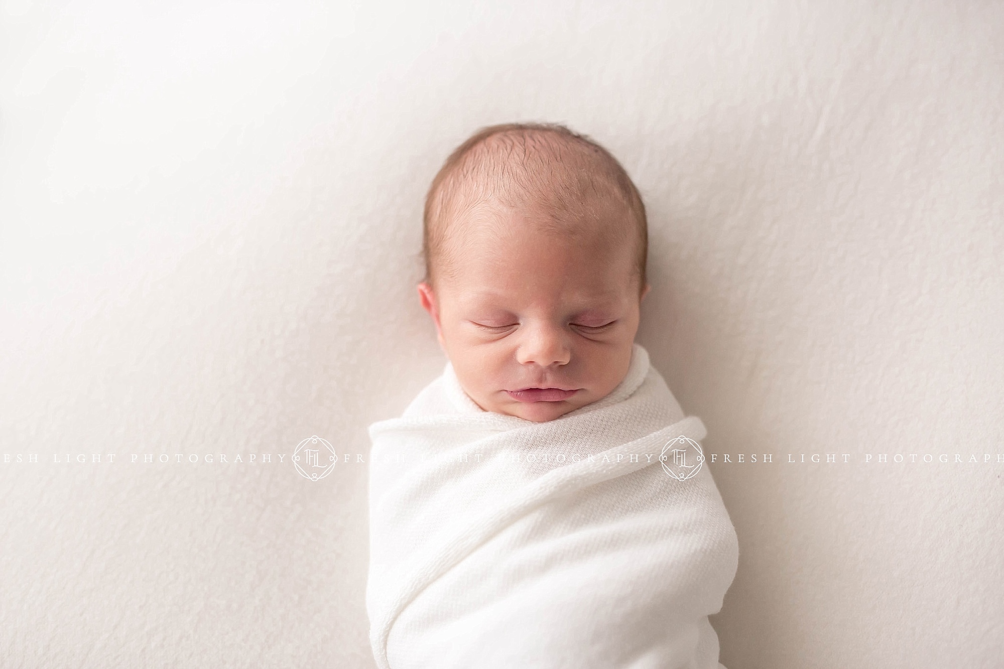 Baby boy swaddled on while blanket in a houston photography studio