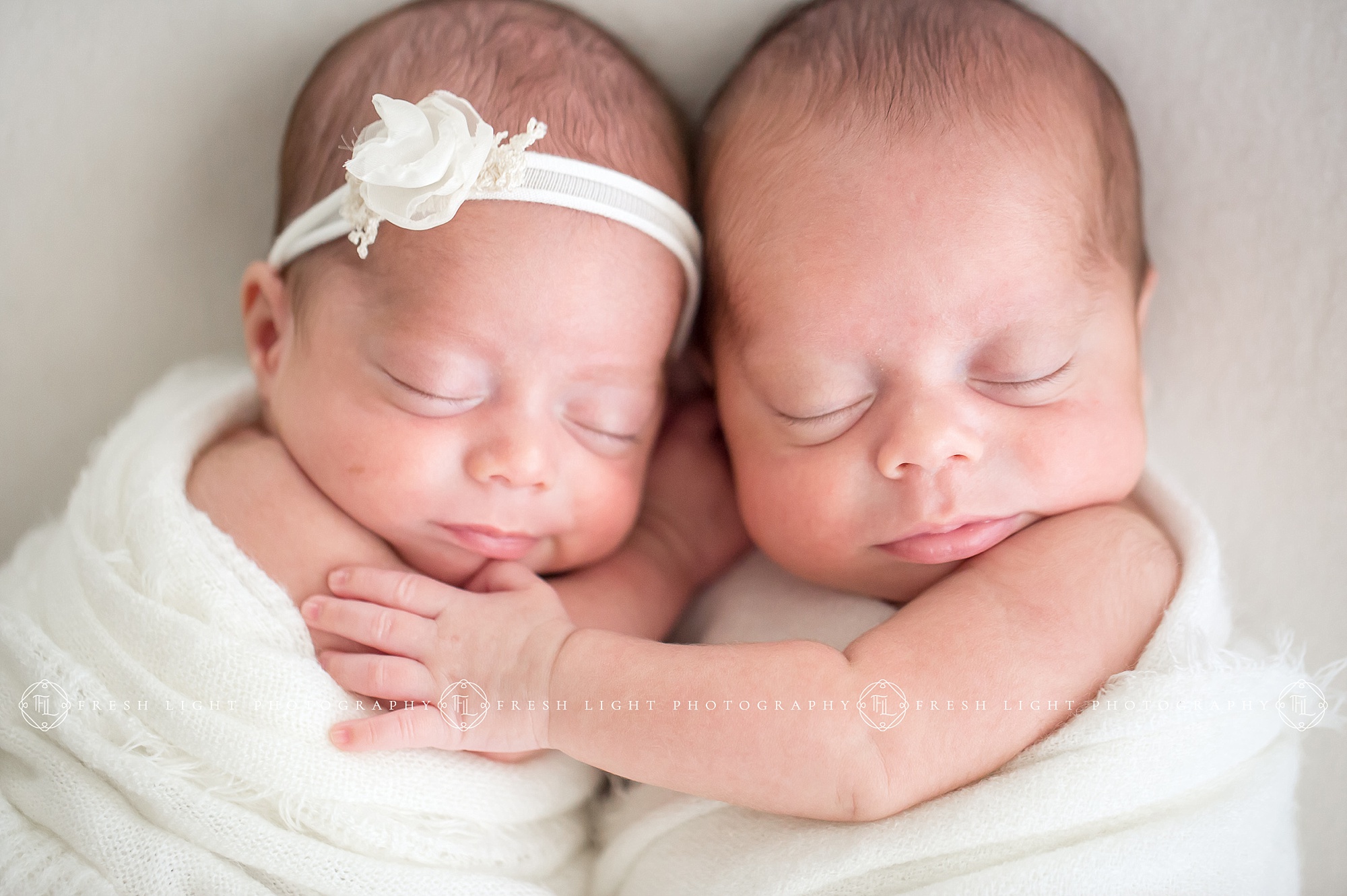 Newborn twins wrapped in blankets holding each other in studio