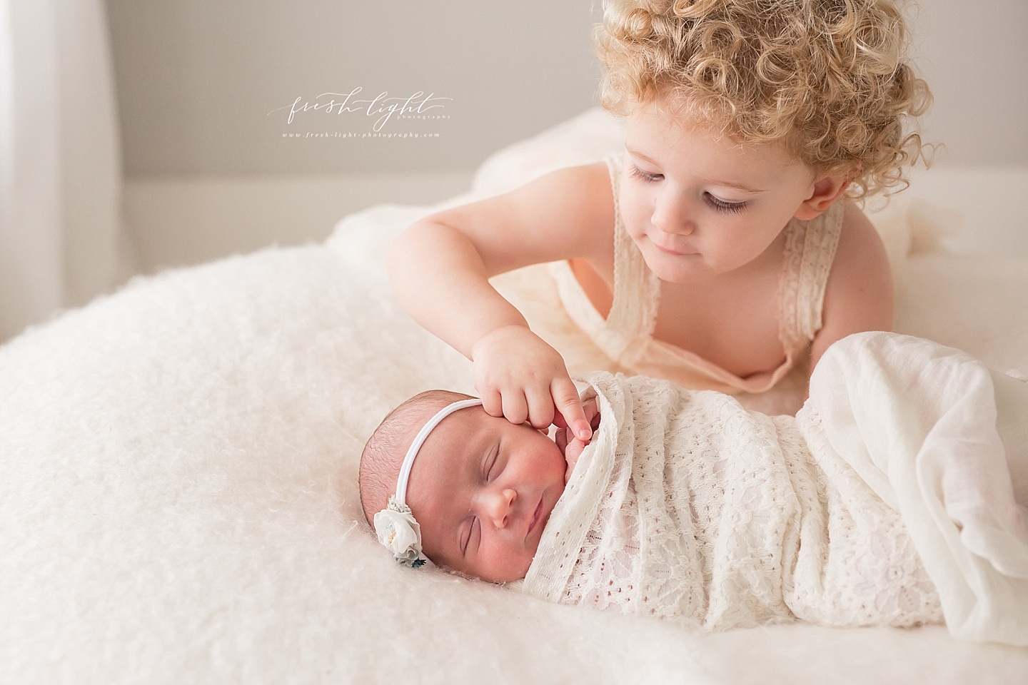 Curly headed girl touches baby sisters fingers