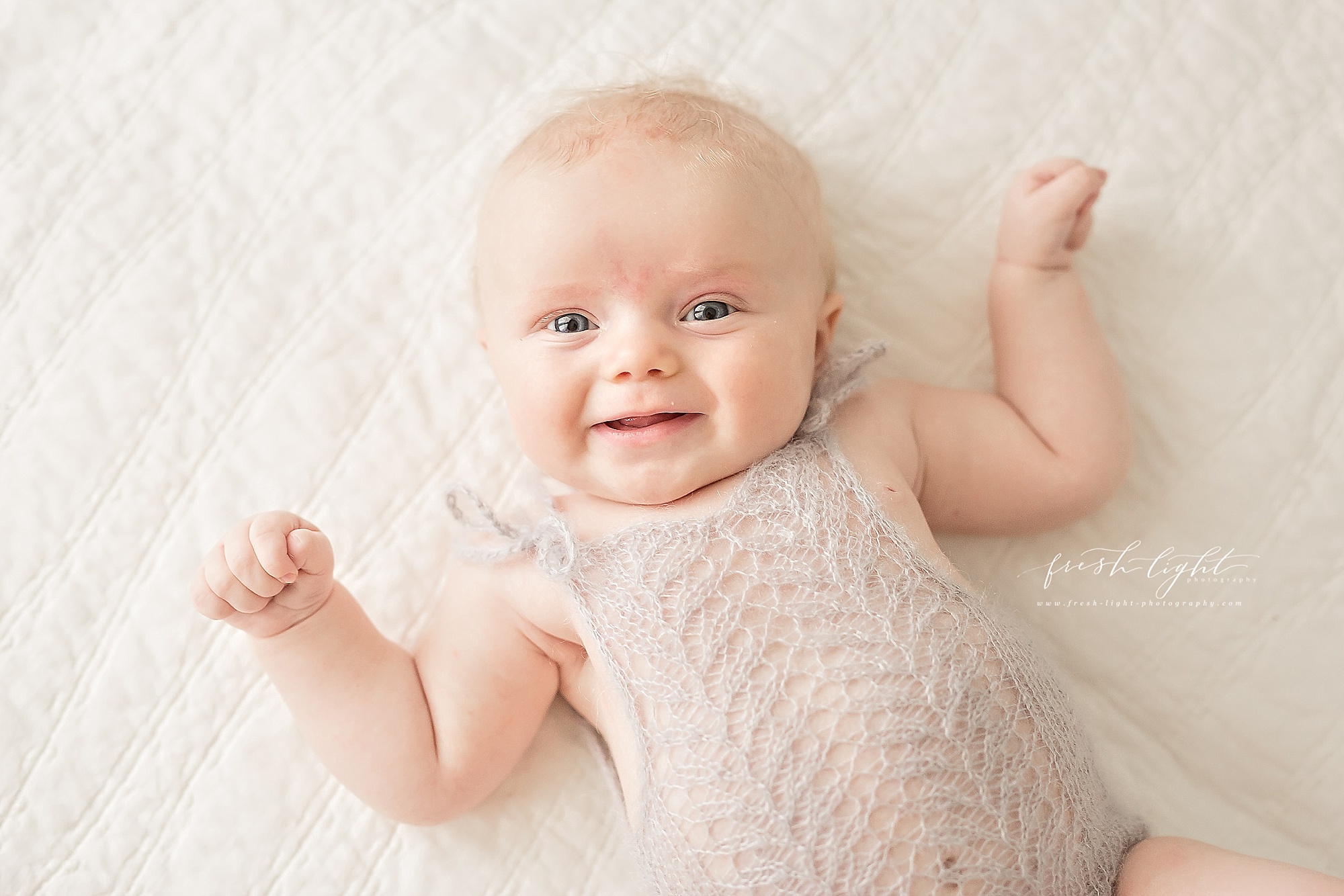 smiling baby on bed in grey knit romper