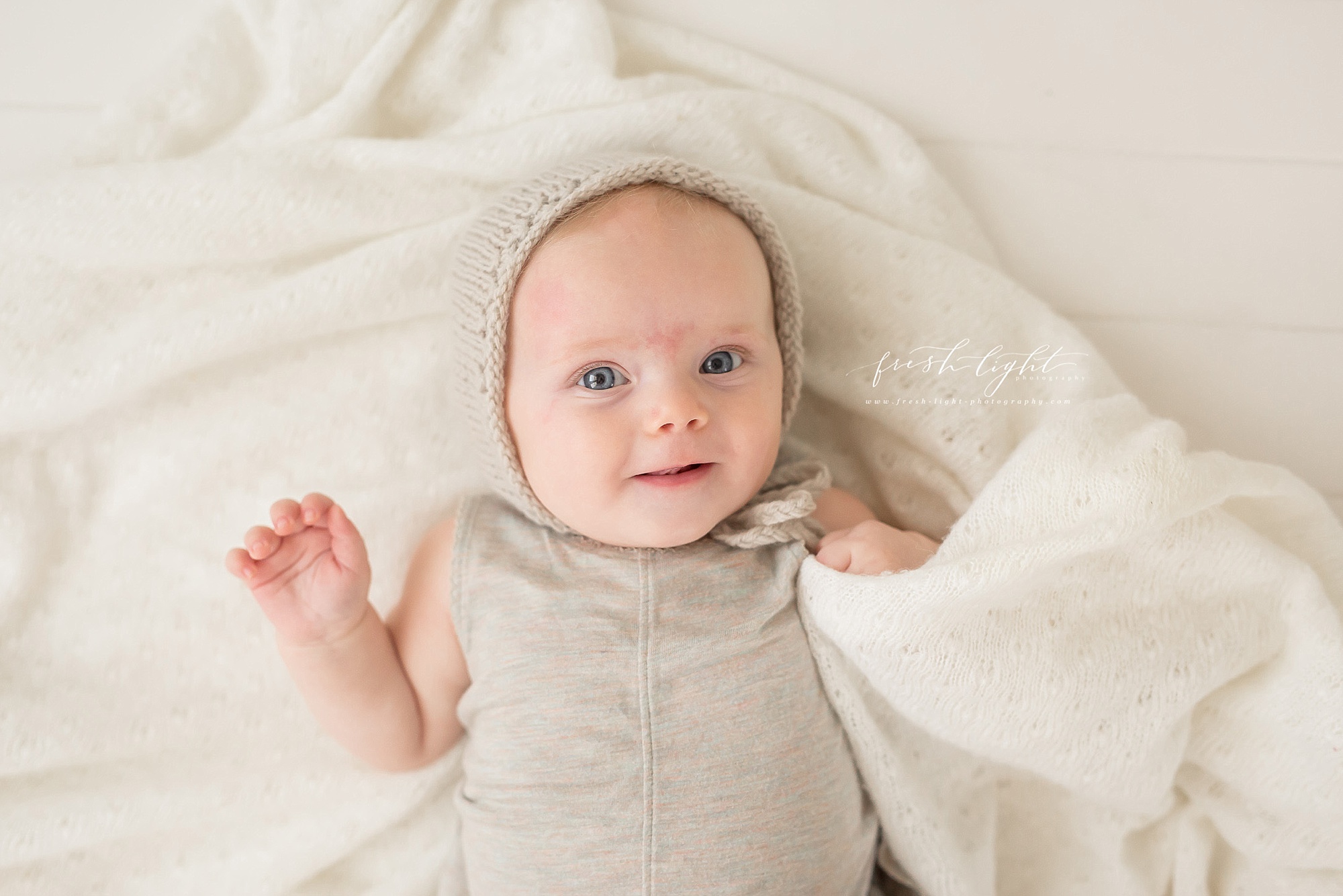 baby in grey bonnet holding a blanket