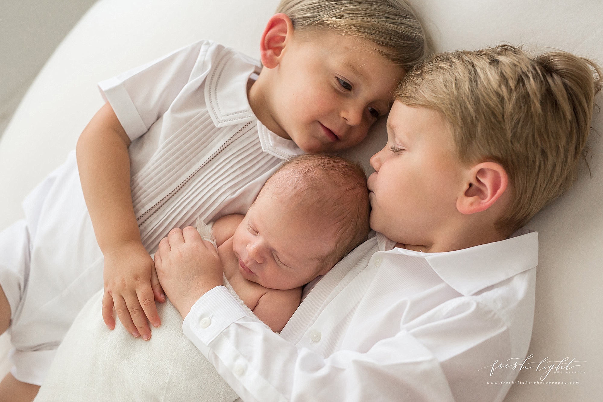 brothers kissing newborn baby's head