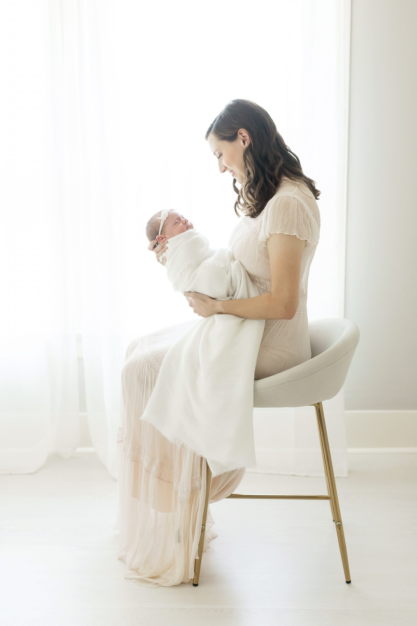 mom sitting on gold stool looking at newborn baby girl