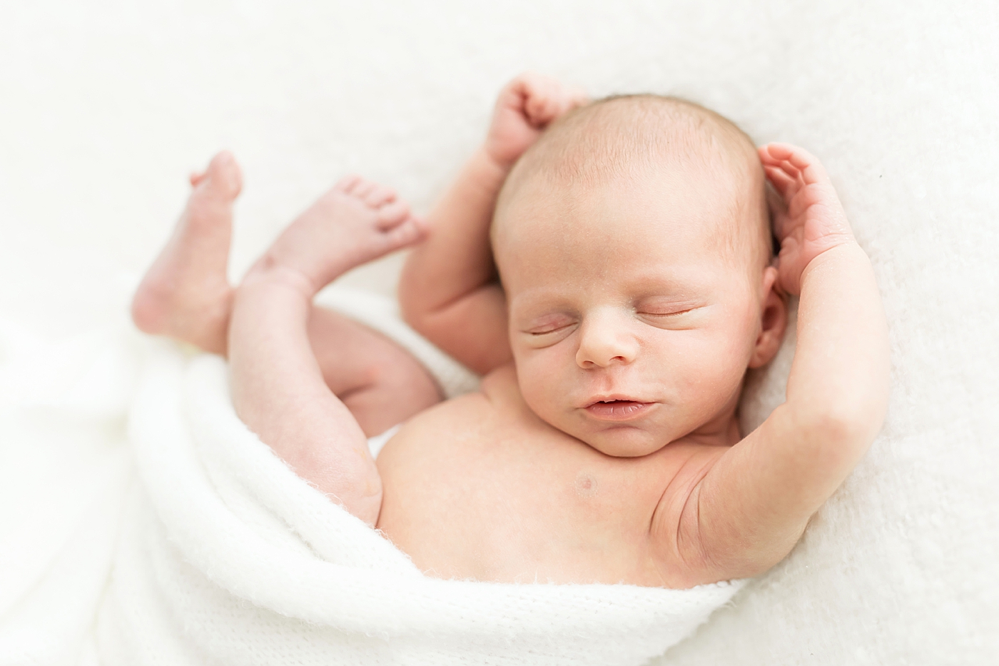 Newborn baby boy curled up on a white blanket for newborn photos with Fresh Light Photography.