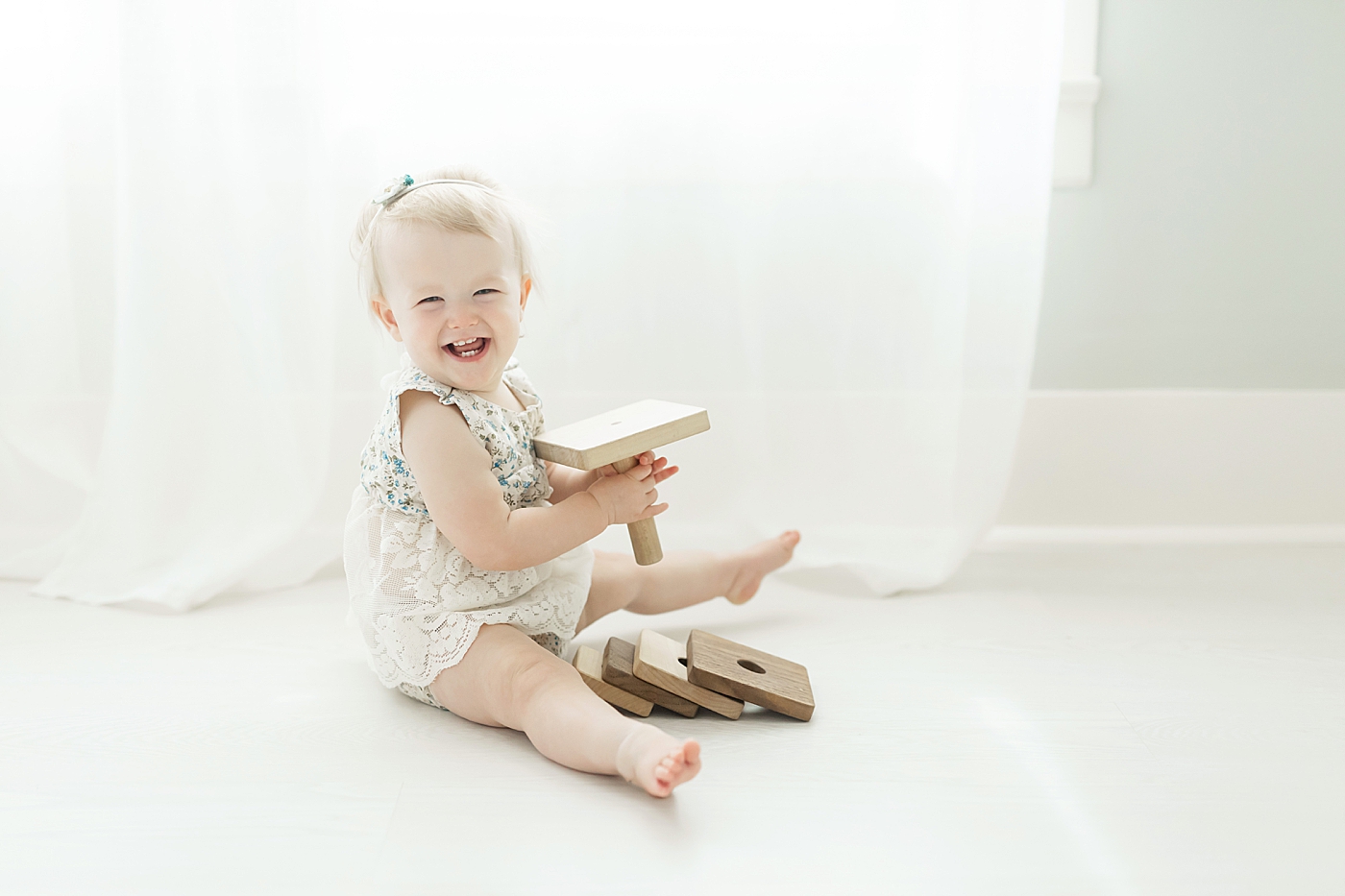 One year old smiling and playing with wooden stacker toy. Photo by Fresh Light Photography.