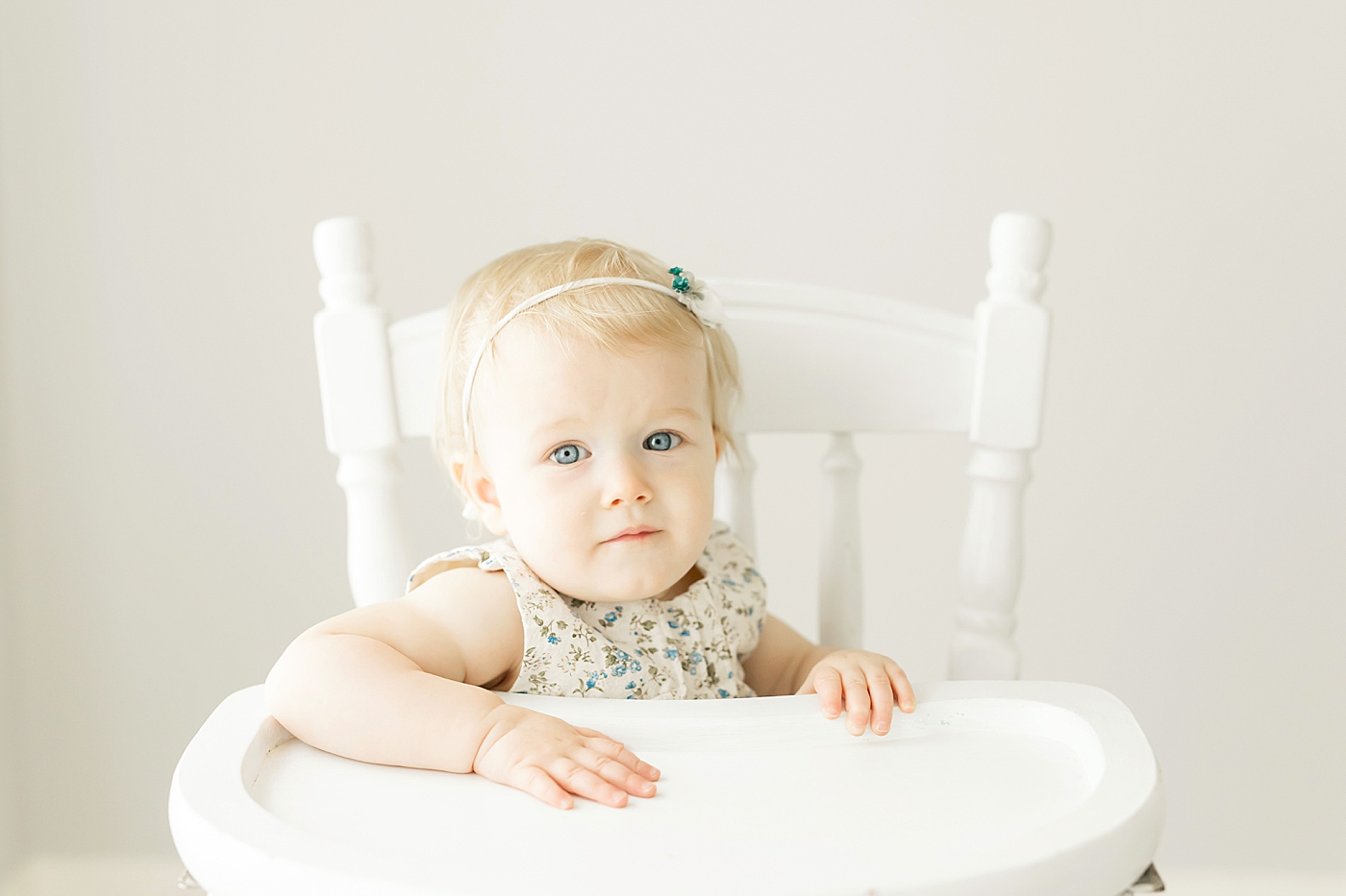 Baby girl with blue eyes sitting in high chair for one year session with Fresh Light Photography.