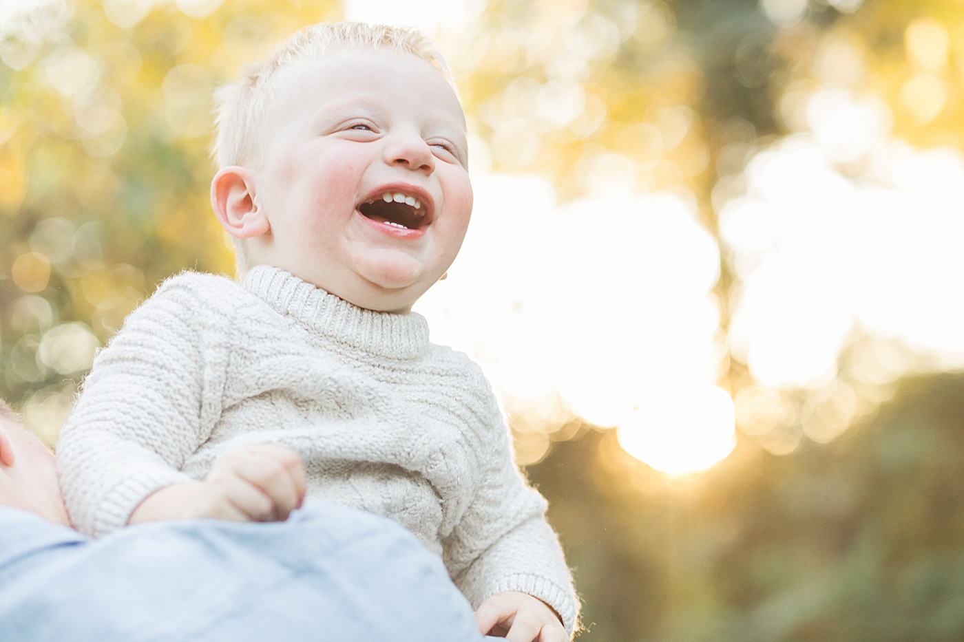 Toddler boy laughing during family photoshoot. He's looking over Dad's shoulder. Photo by Fresh Light Photography