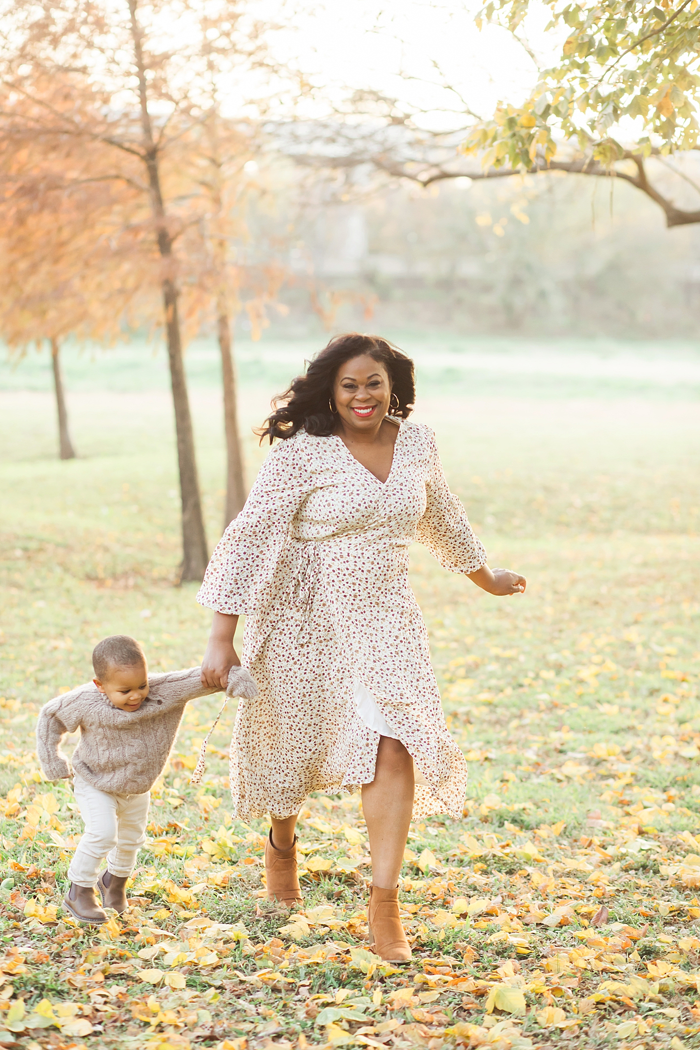 Mom and son running through the park during fall with the leaves on the ground. Photo by Fresh Light Photography.