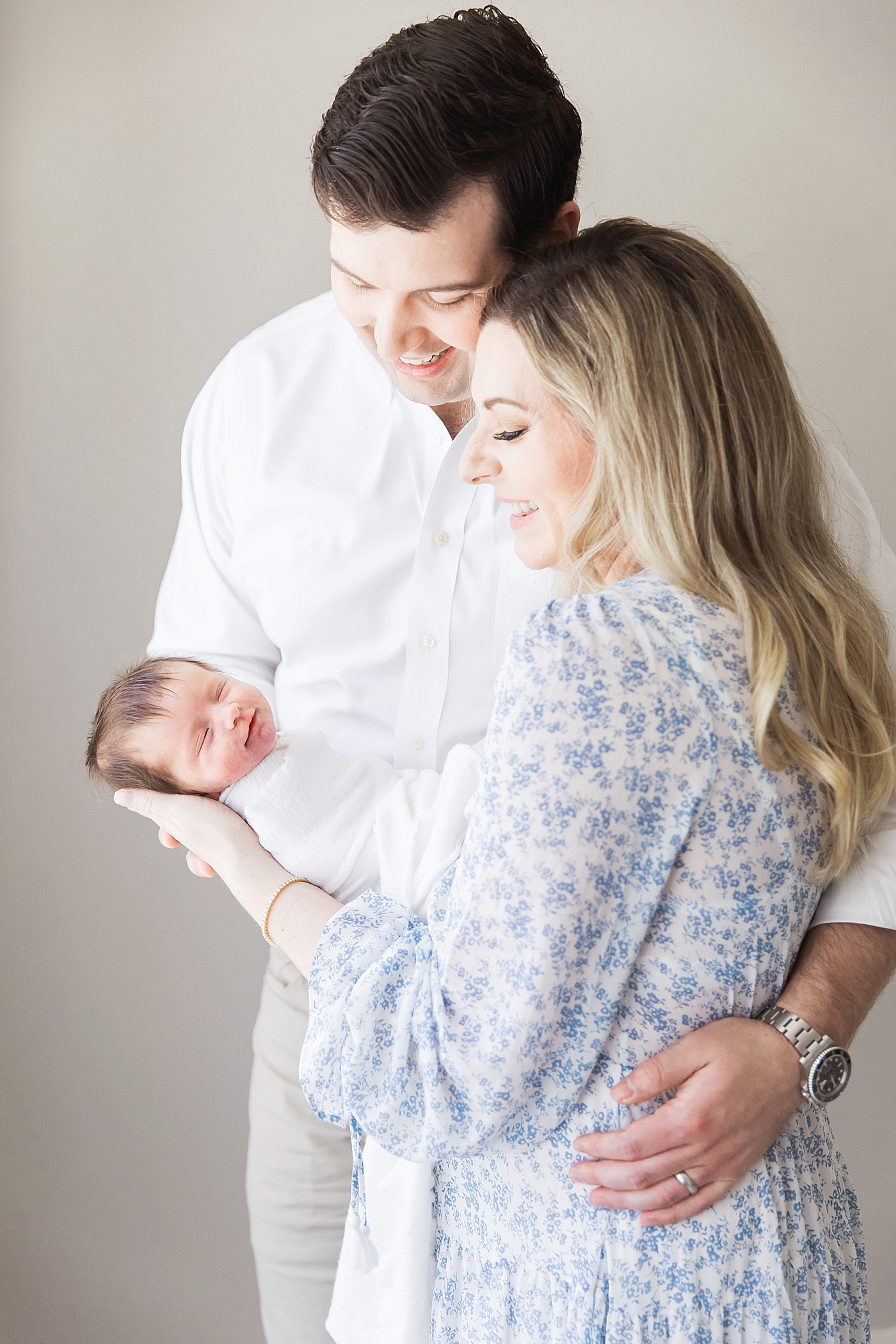 Mom and Dad holding their daughter and she smiles during newborn photoshoot with Fresh Light Photography.