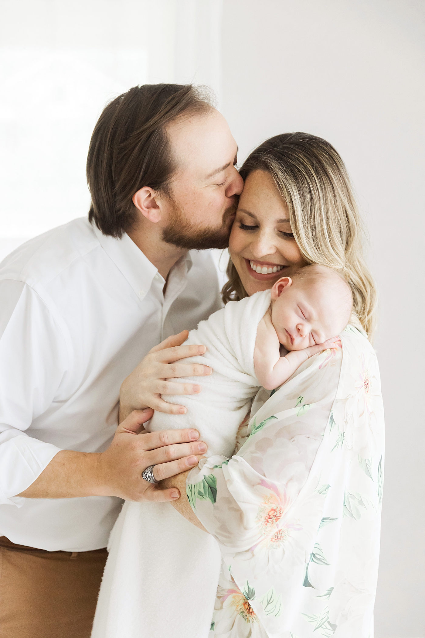Dad kissing Mom while she holds their baby boy. Photo by Fresh Light Photography.