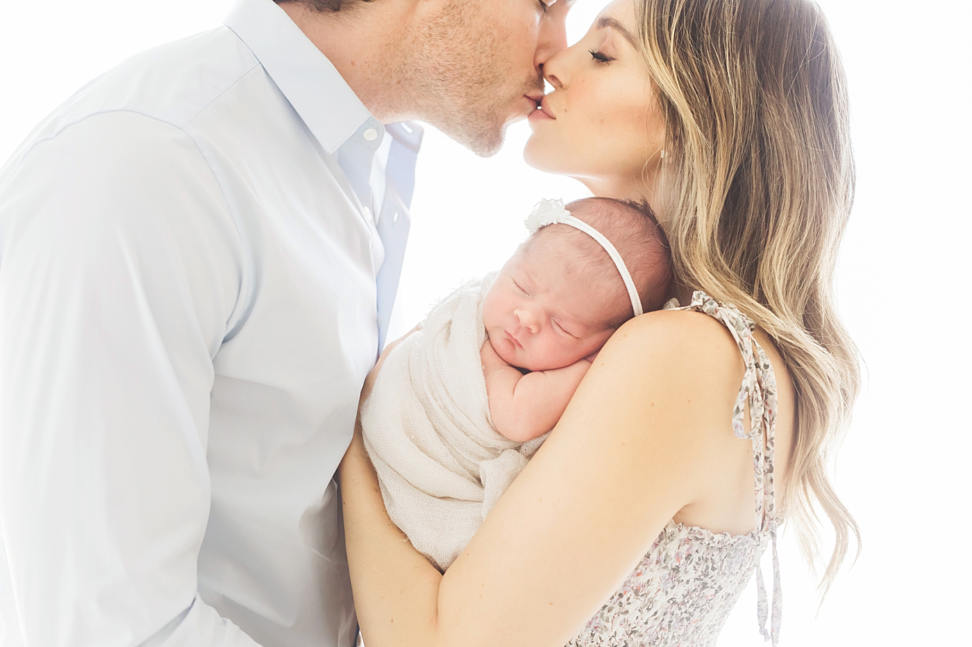 Mom and Dad kissing over their newborn baby girl. Photo by Fresh Light Photography