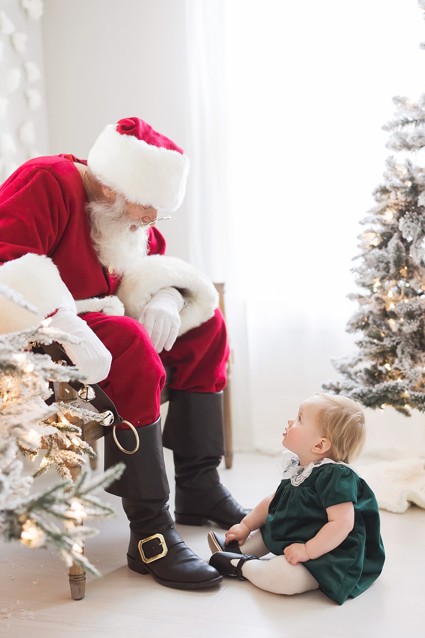 Baby girl sitting on floor looking up at Santa. Photo by Fresh Light Photography.