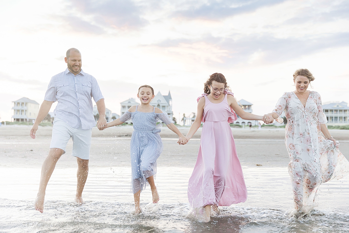 Family of four running into the water during family session on Galveston beach. Photo by Fresh Light Photography.