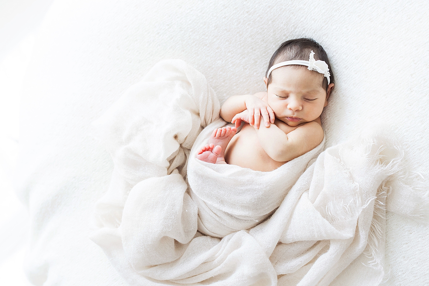 Newborn baby girl curled up in swaddle blanket. Photo by Fresh Light Photography.