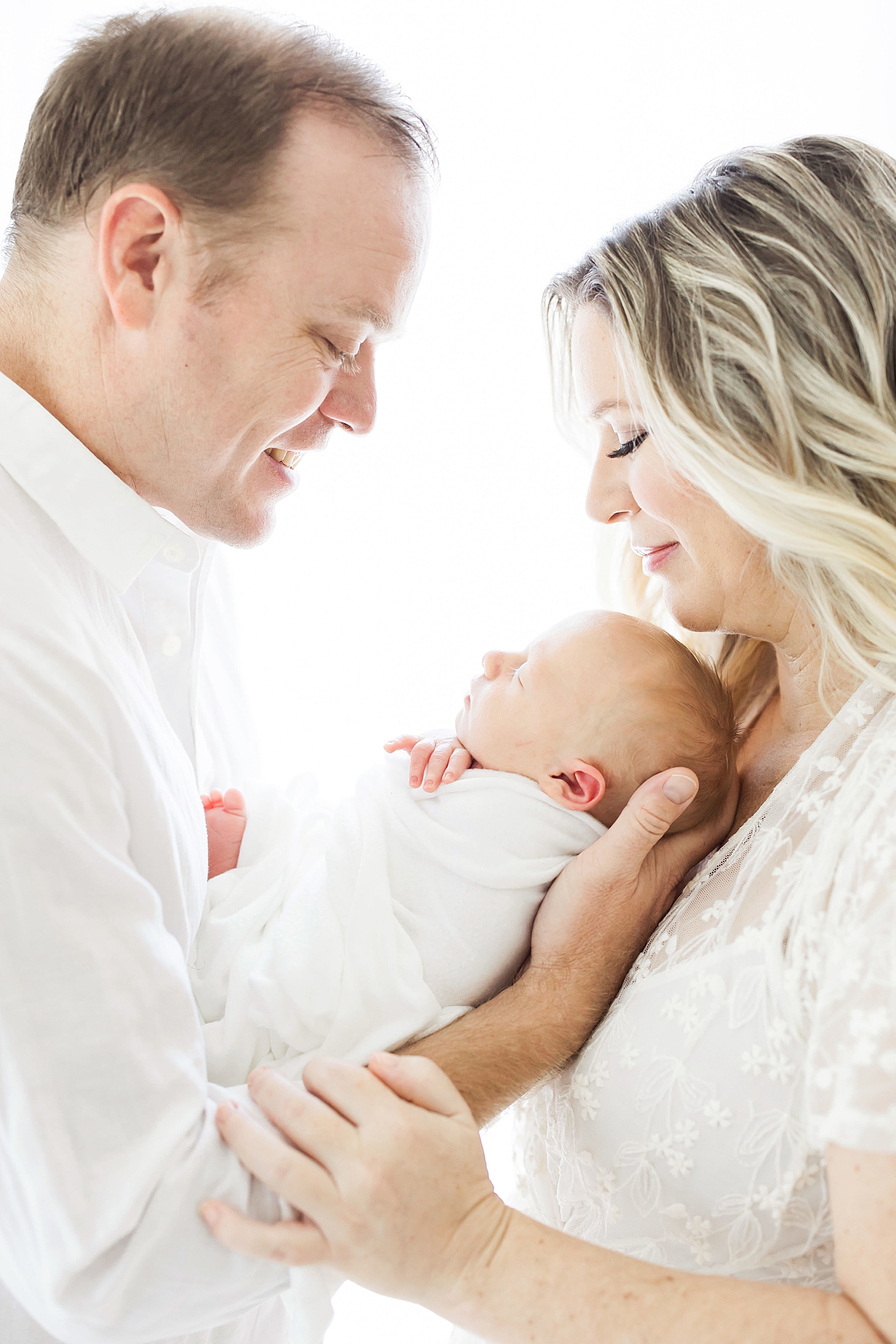 Parents holding their baby boy looking down at him. Photo by Fresh Light Photography.