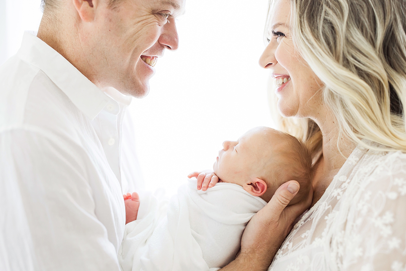 Parents looking at each other and smiling as they hold their newborn son. Photo by Fresh Light Photography.
