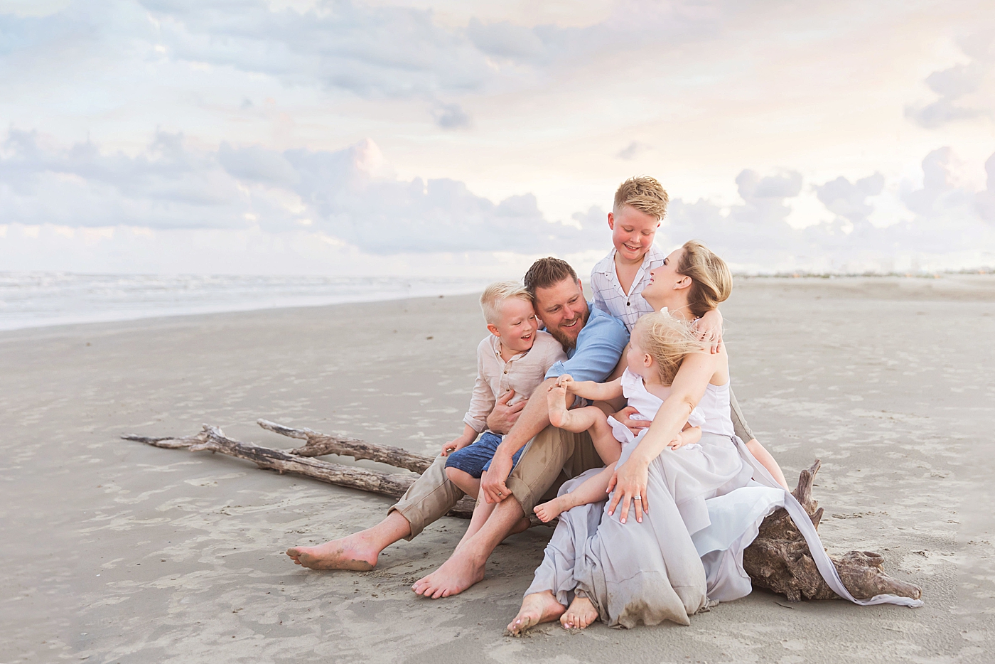 Family sitting on driftwood during photoshoot on the beach in Galveston. Photo by Fresh Light Photography