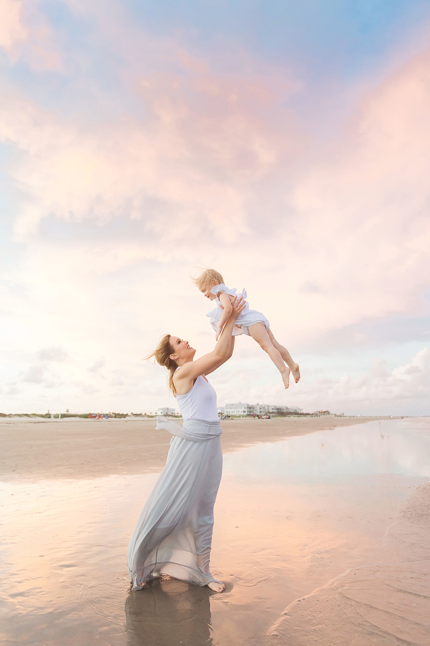Mom holding baby girl up in the air on the beach during family photos. Photo by Fresh Light Photography
