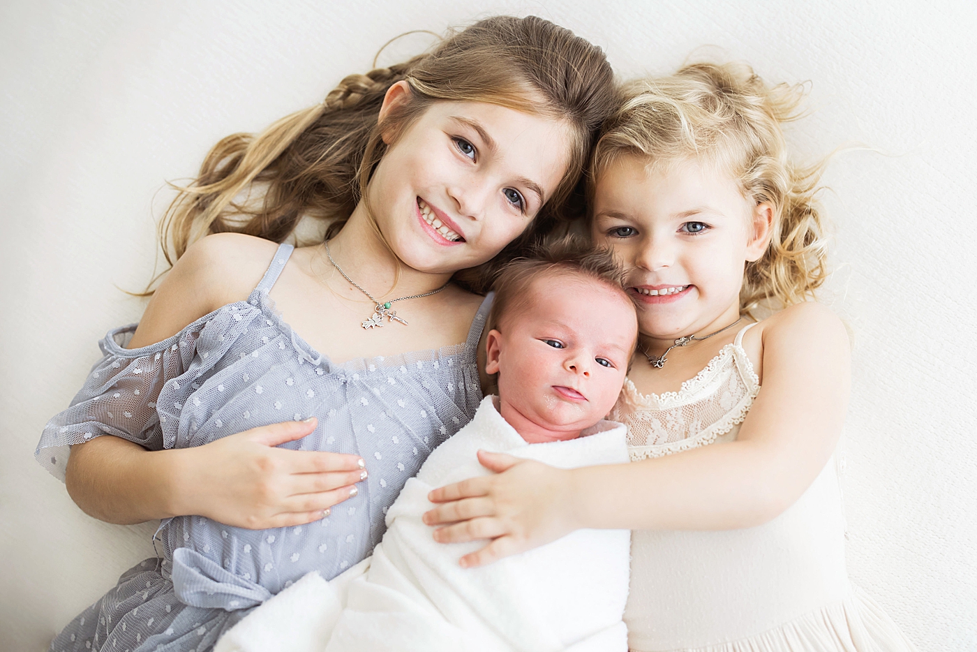 Two big sisters holding their baby brother. Photo by Fresh Light Photography.