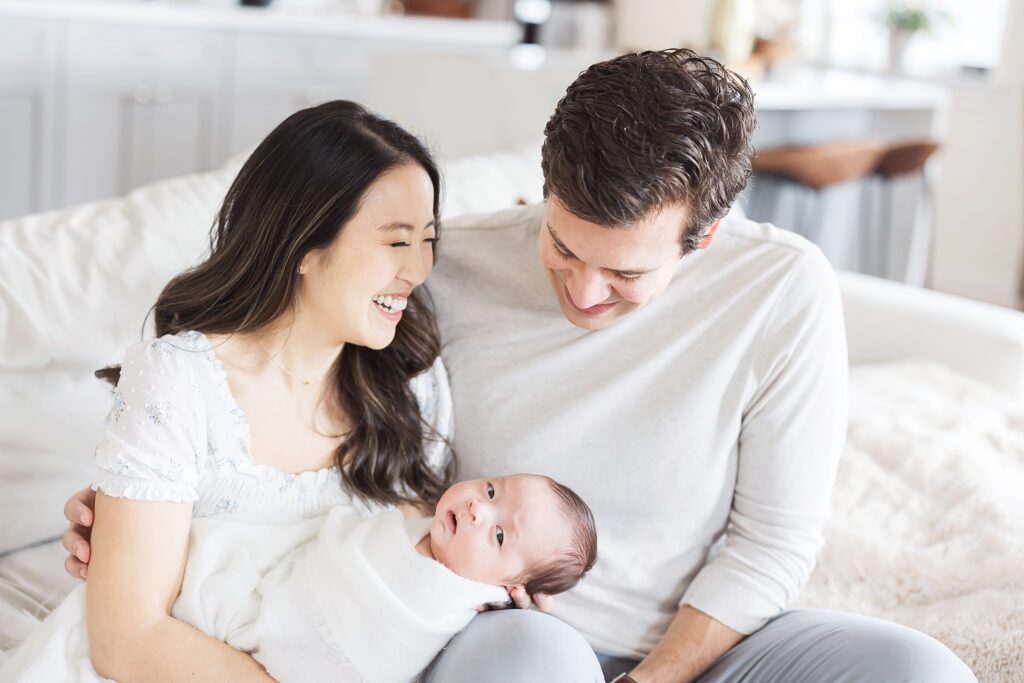 Intimate family moment captured in a light and airy setting, featuring a newborn baby cradled in the loving embrace of their parents.