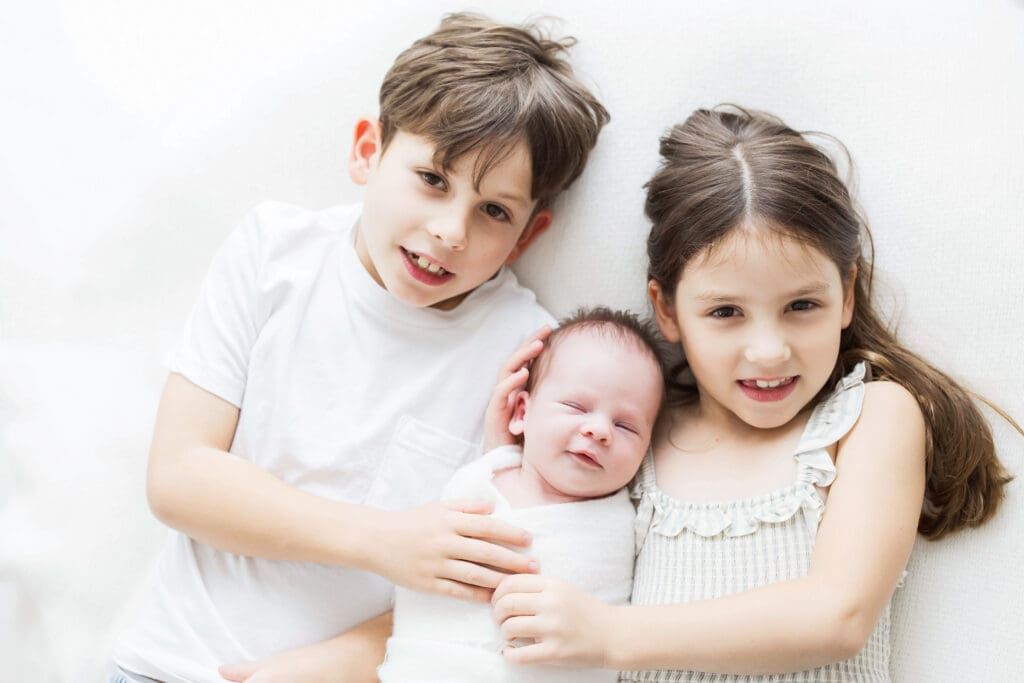 Brother and sister cuddling their newborn baby sibling during a professional newborn photography session in Houston, Texas