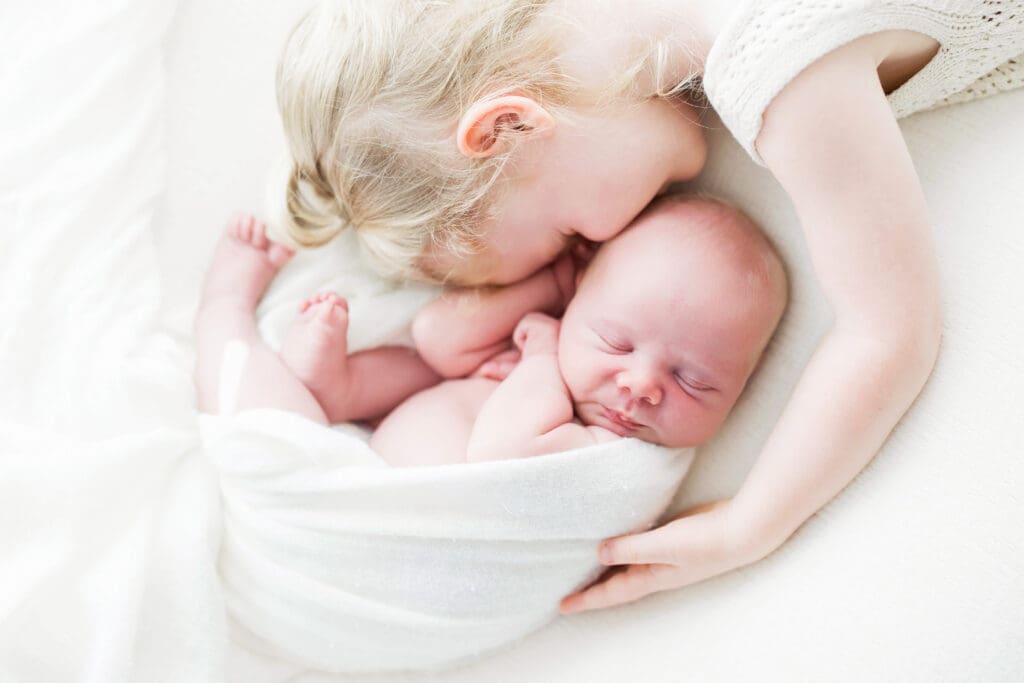 Older sister sharing a sweet moment with her newborn sibling during a newborn family photography session in Houston Heights, TX.