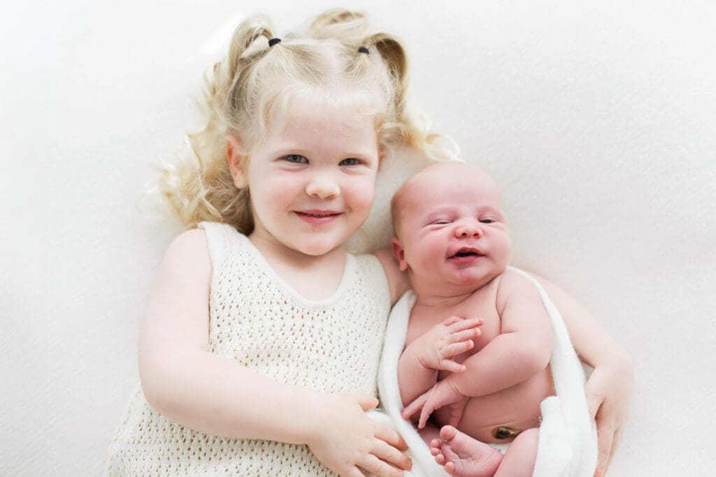 Elder sister gently holding and cuddling her newborn sibling during a heartwarming family photography session in Houston Heights, TX.